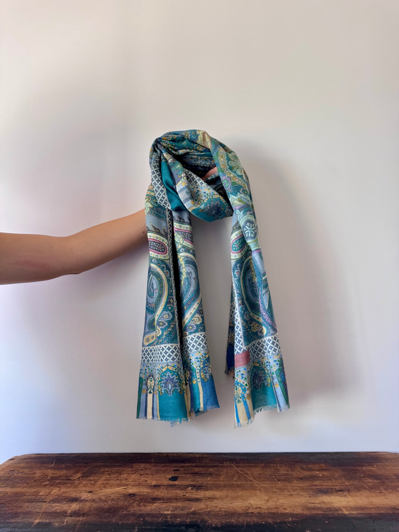 Blue patterned scarf held by a hand on a wooden surface with a white background