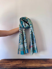 Blue patterned scarf held by a hand on a wooden surface with a white background
