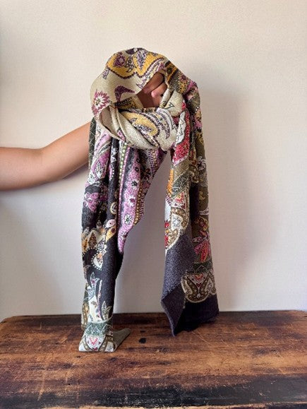 Person wearing a colorful patterned scarf on a wooden surface with a plain background