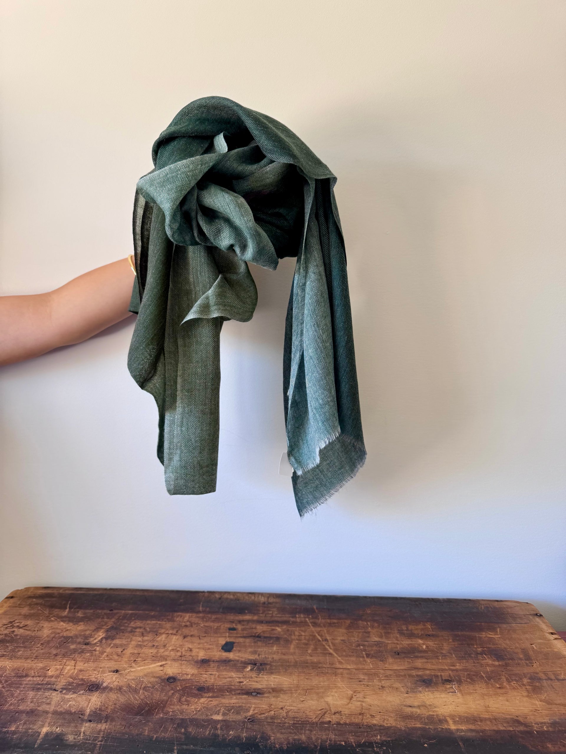 Green towel held above a wooden surface with a plain background