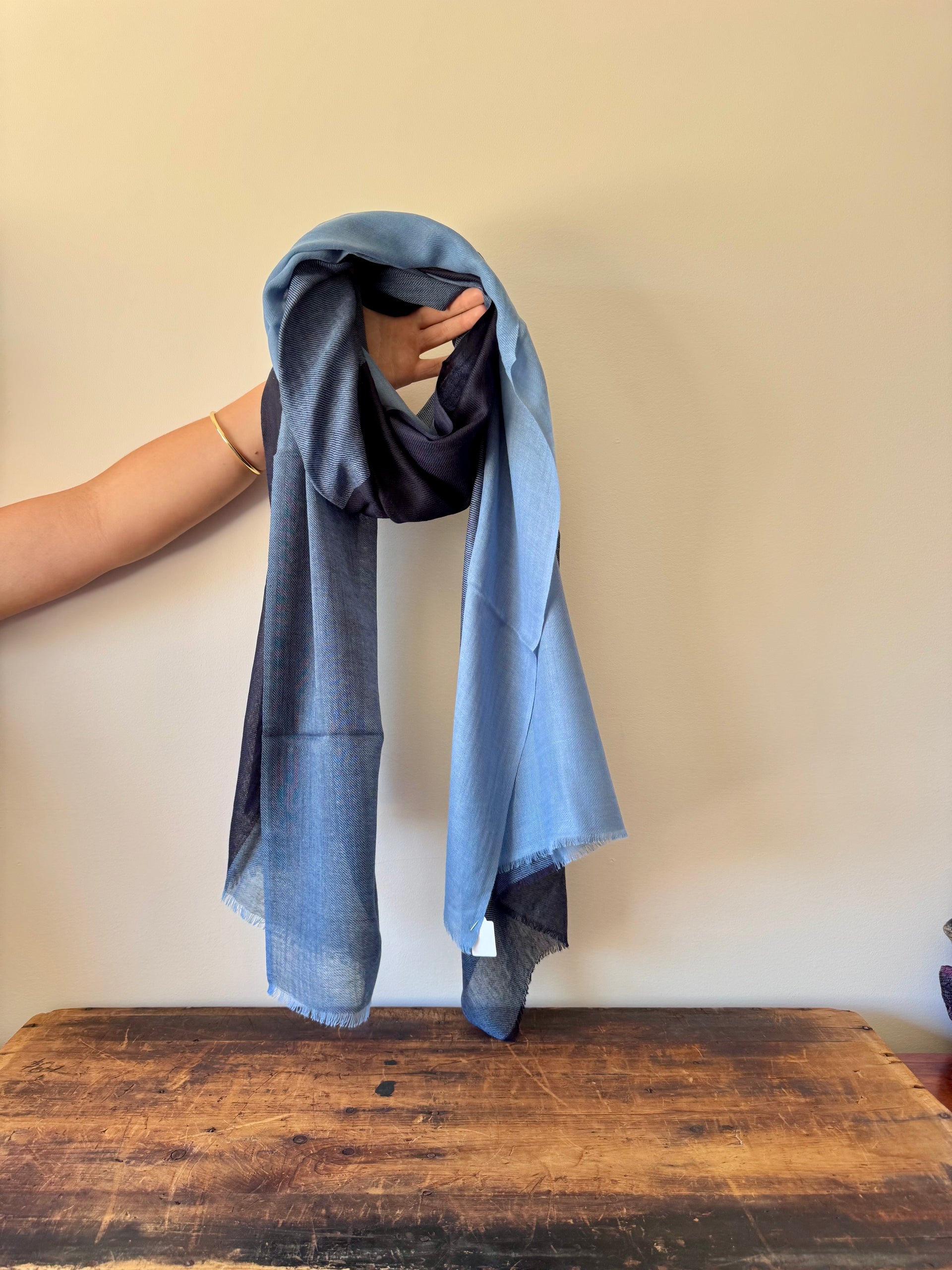 Person holding a blue scarf over a wooden surface with a plain background