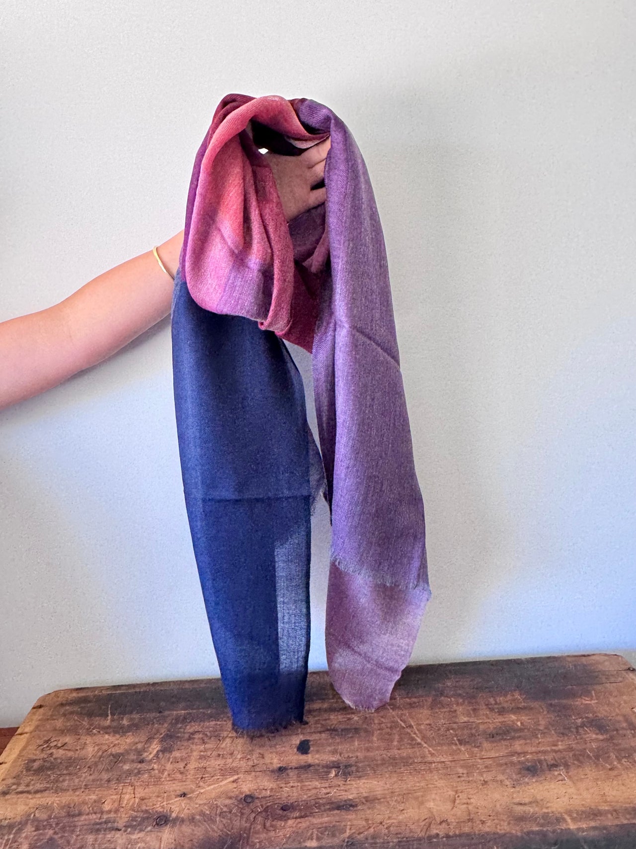 Person holding a gradient scarf on a wooden surface with a white background