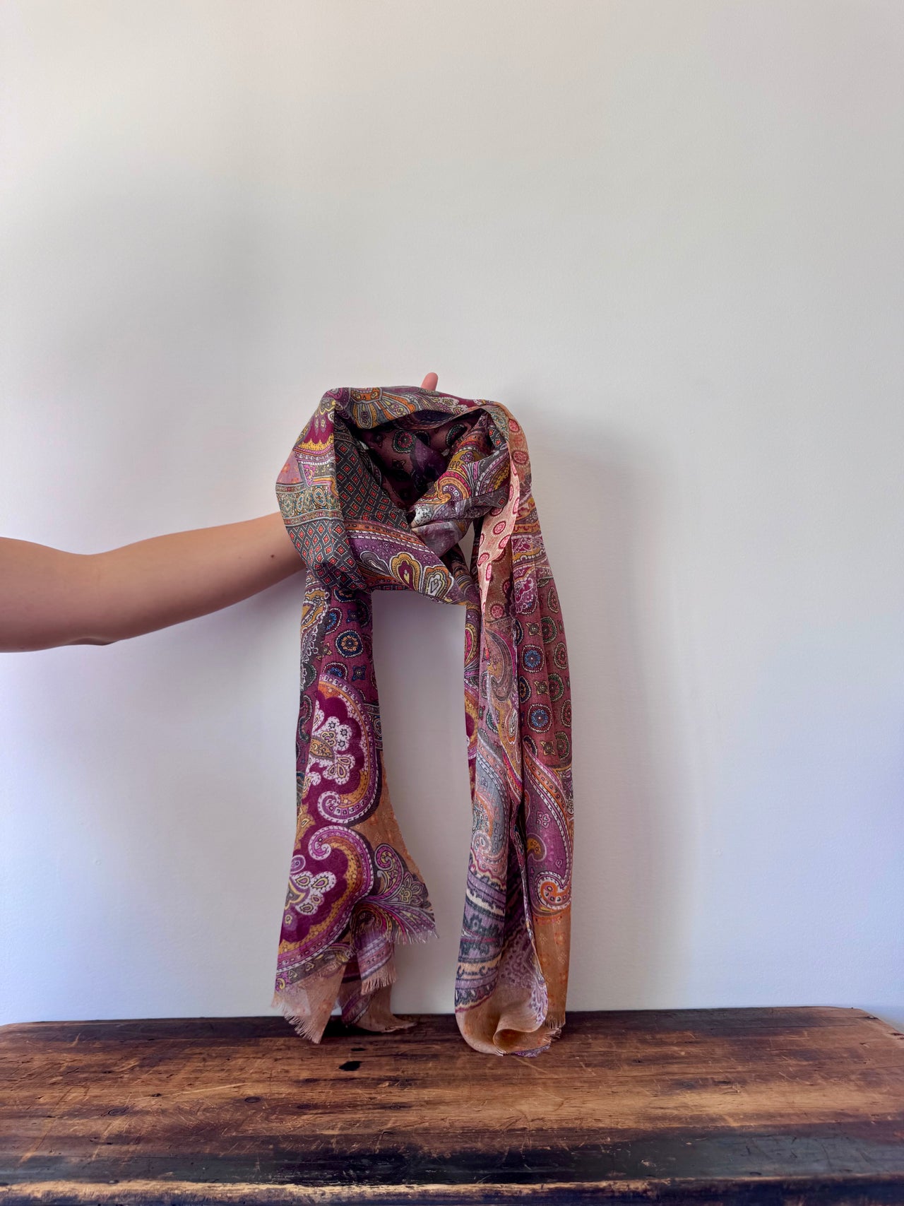 Person holding a patterned scarf on a wooden surface with a white background
