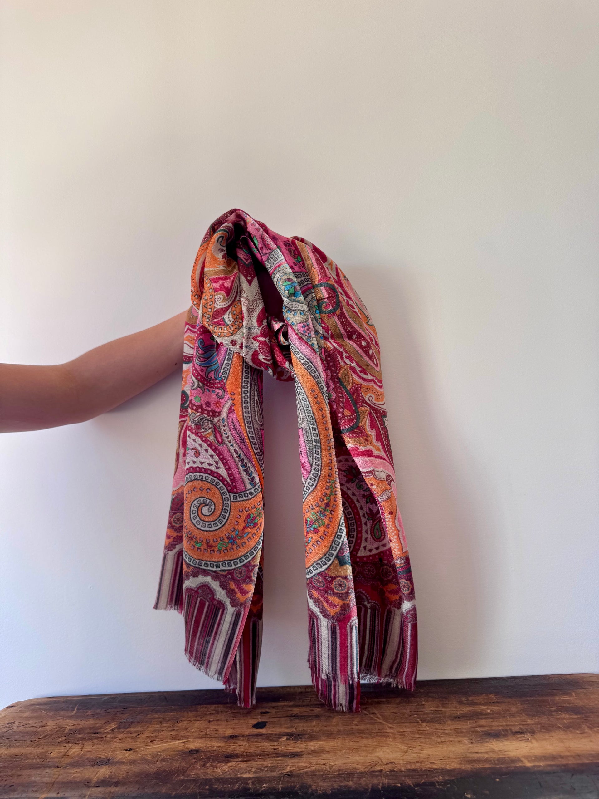 Colorful patterned scarf held by a person against a white wall.