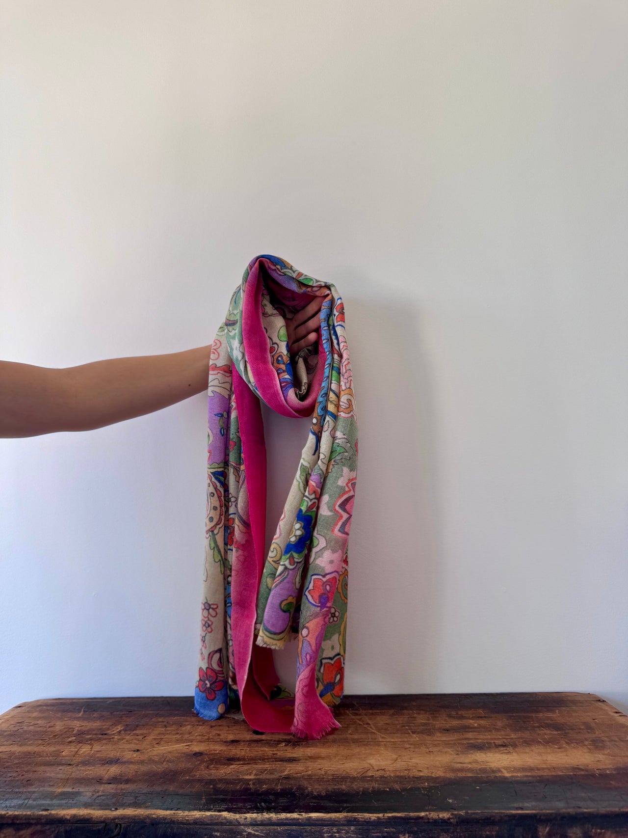 Colorful patterned scarf held by a person on a wooden surface with a white background