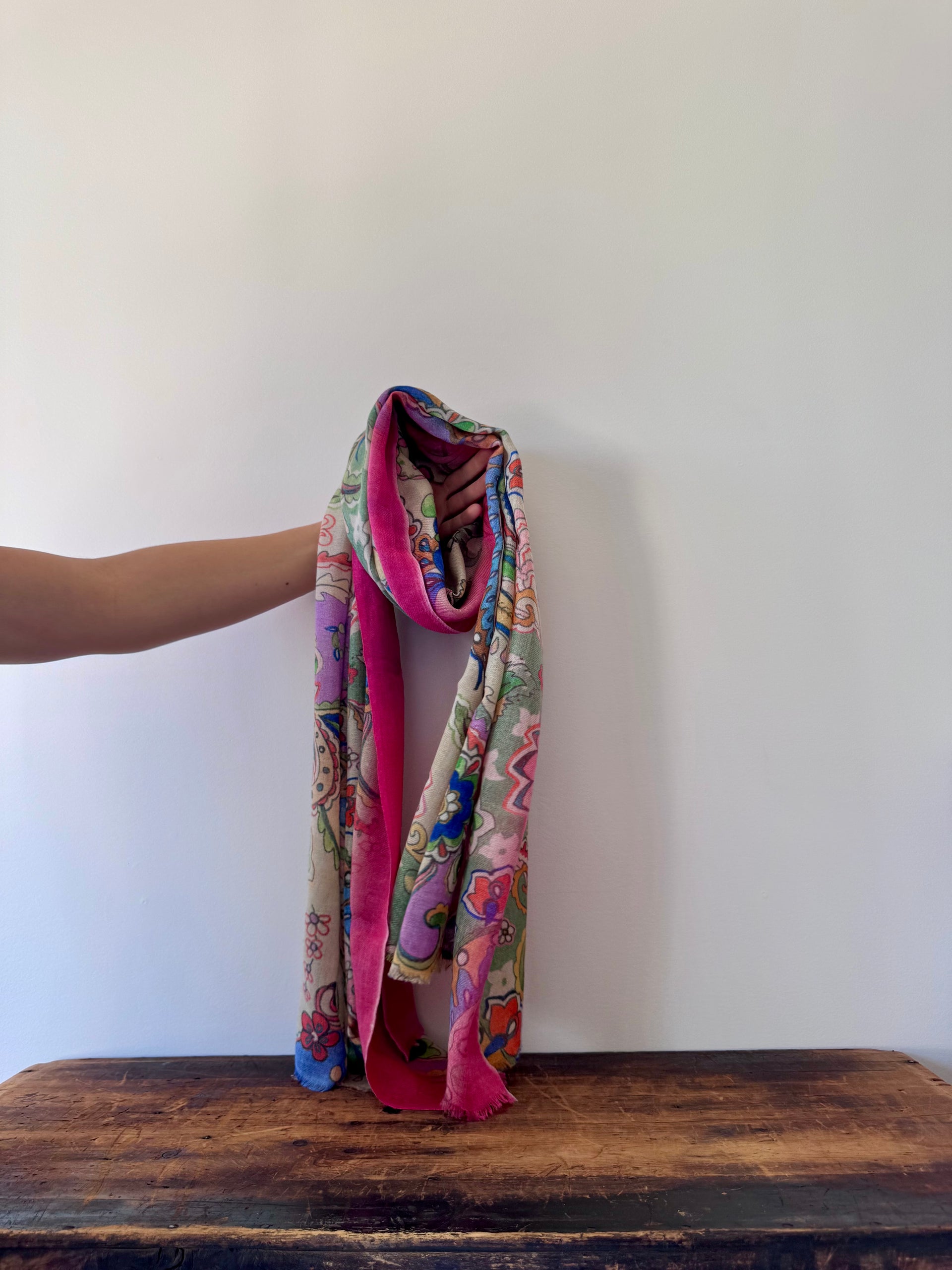 Colorful patterned scarf held by a person on a wooden surface with a white background