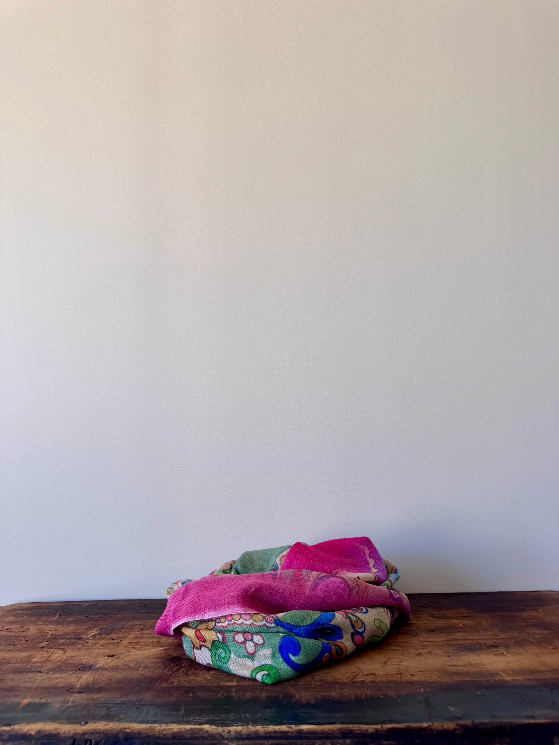 Colorful fabric folded on a wooden surface with a white wall background