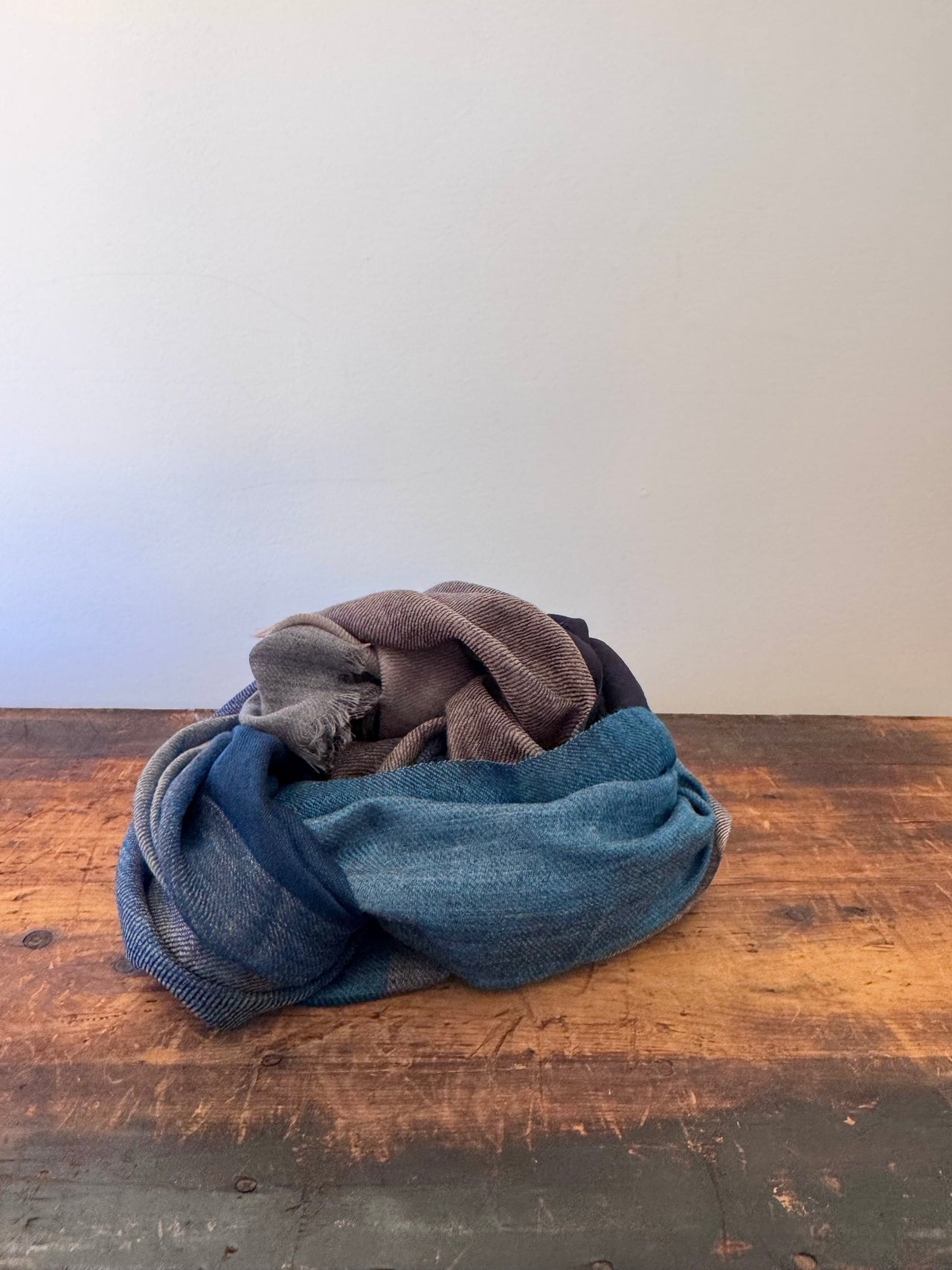 Stack of folded jeans on a wooden surface with a white wall background