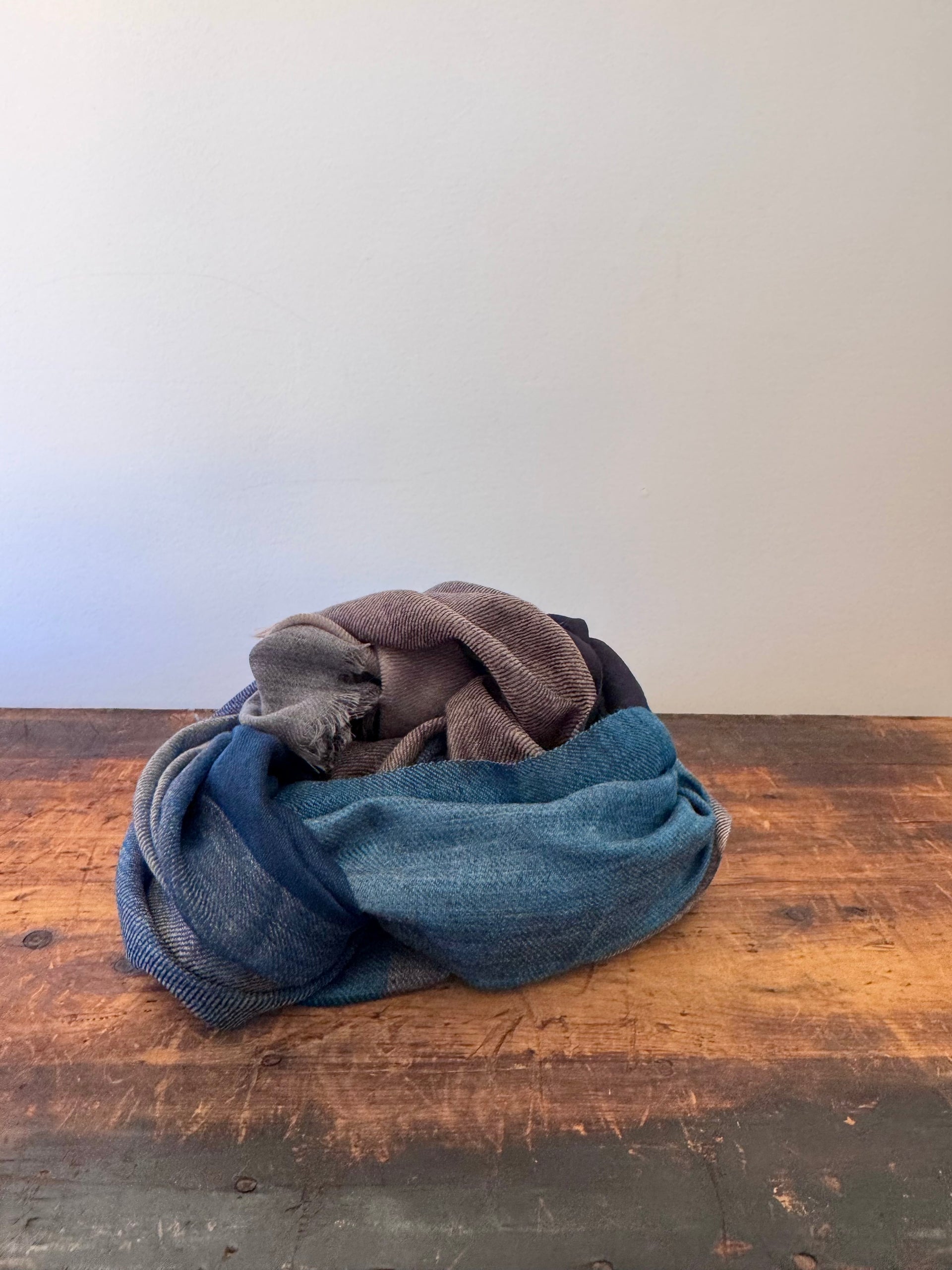 Stack of folded jeans on a wooden surface with a white wall background