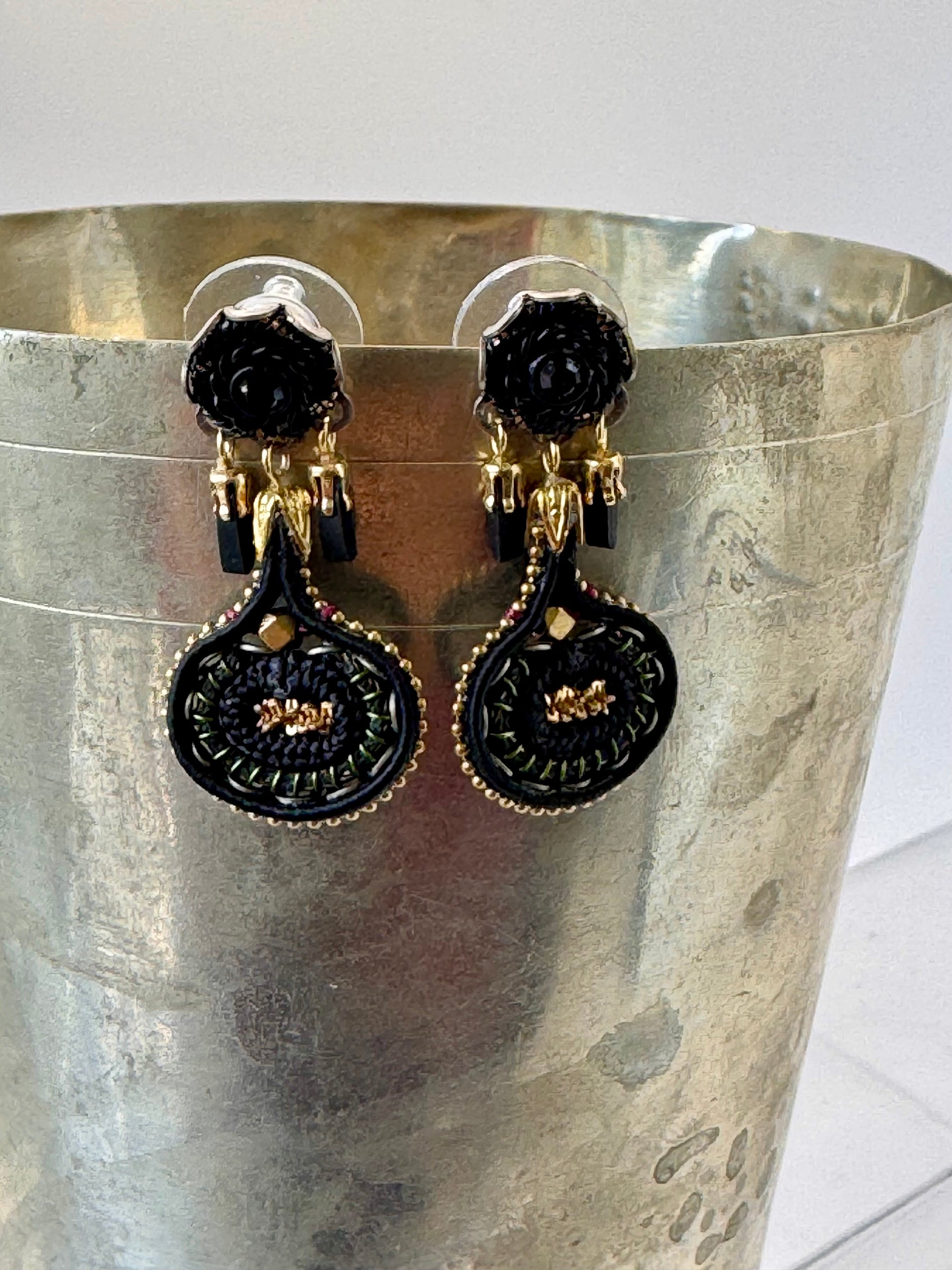 Black and gold earrings on a metallic stand against a white background