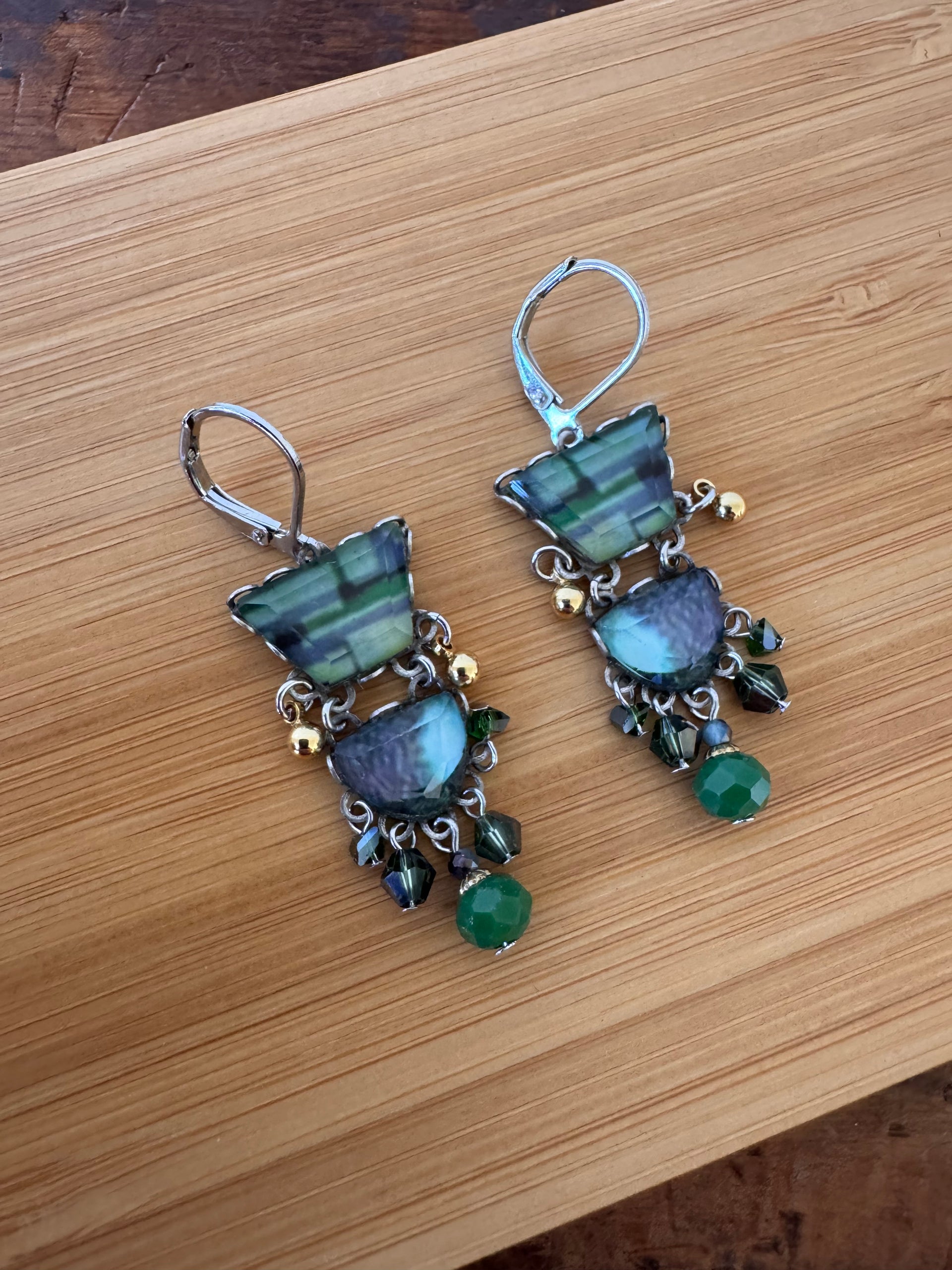 Pair of earrings with green and blue stones on a wooden surface