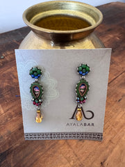 Pair of earrings on a 'Ayala' branded card with a brass container in the background.