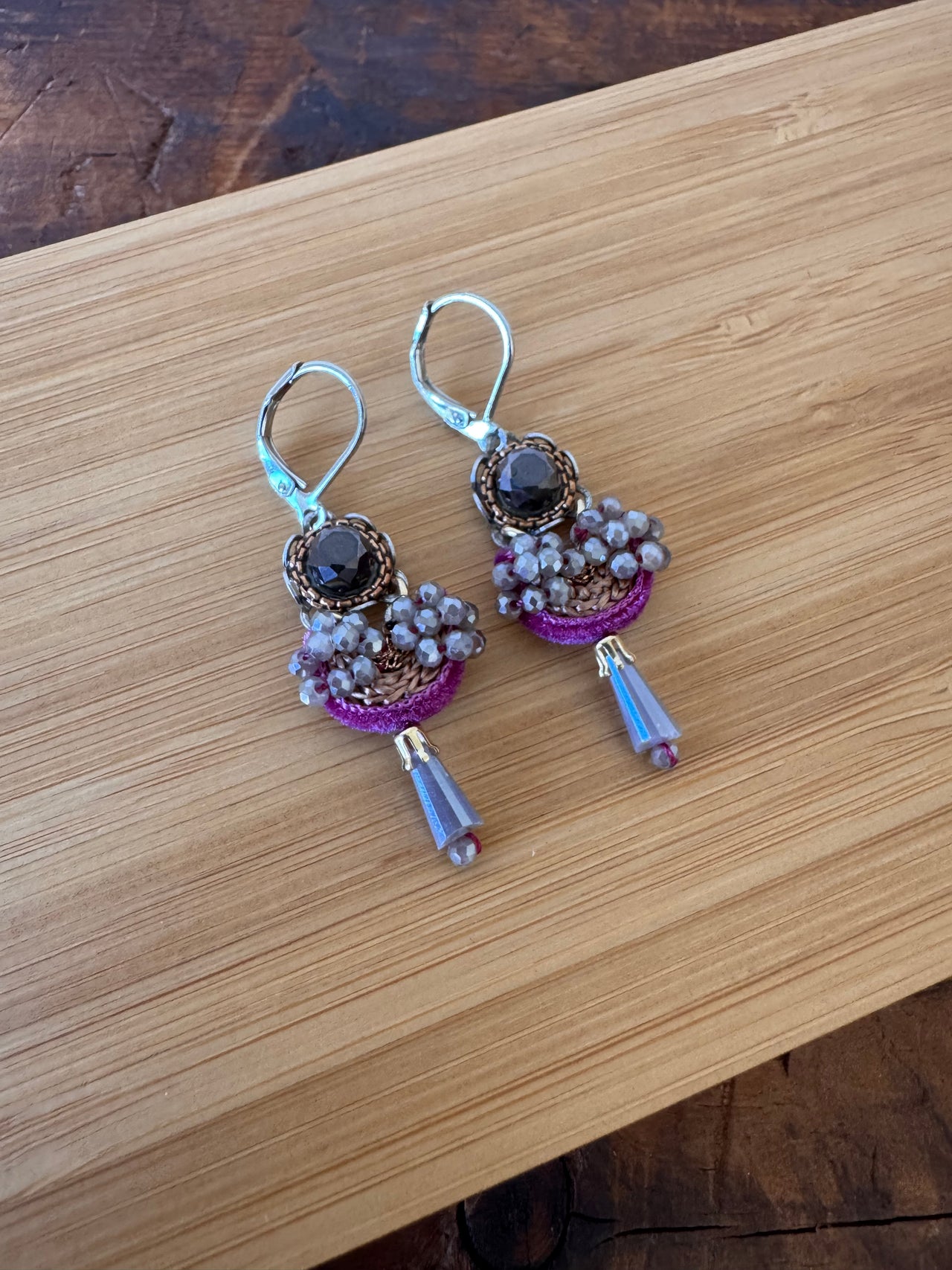 Pair of earrings with purple and gold accents on a wooden surface