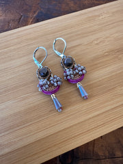 Pair of earrings with purple and gold accents on a wooden surface