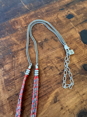 Two necklaces on a wooden surface, one with a chain and the other with a colorful pattern.