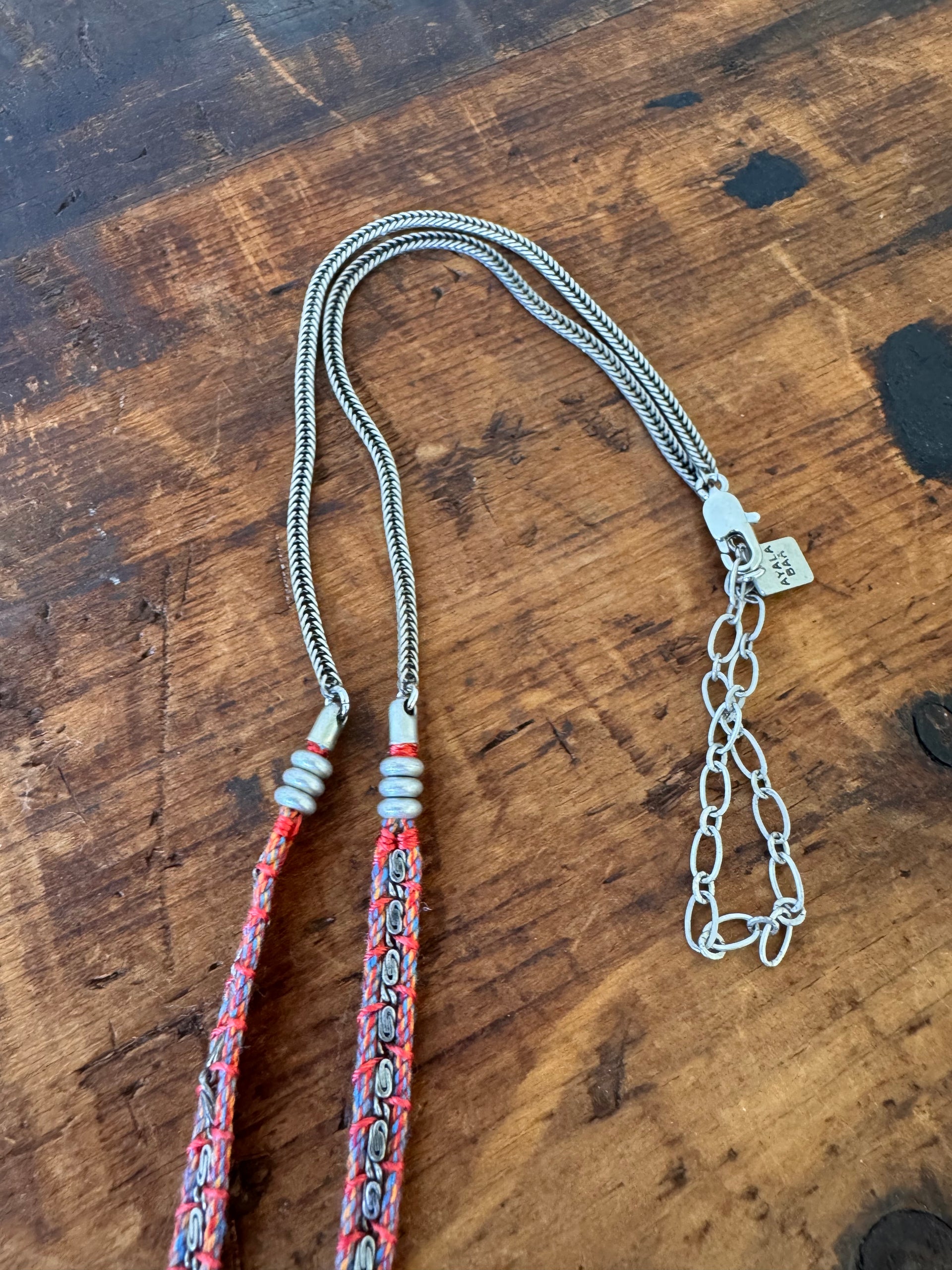 Two necklaces on a wooden surface, one with a chain and the other with a colorful pattern.