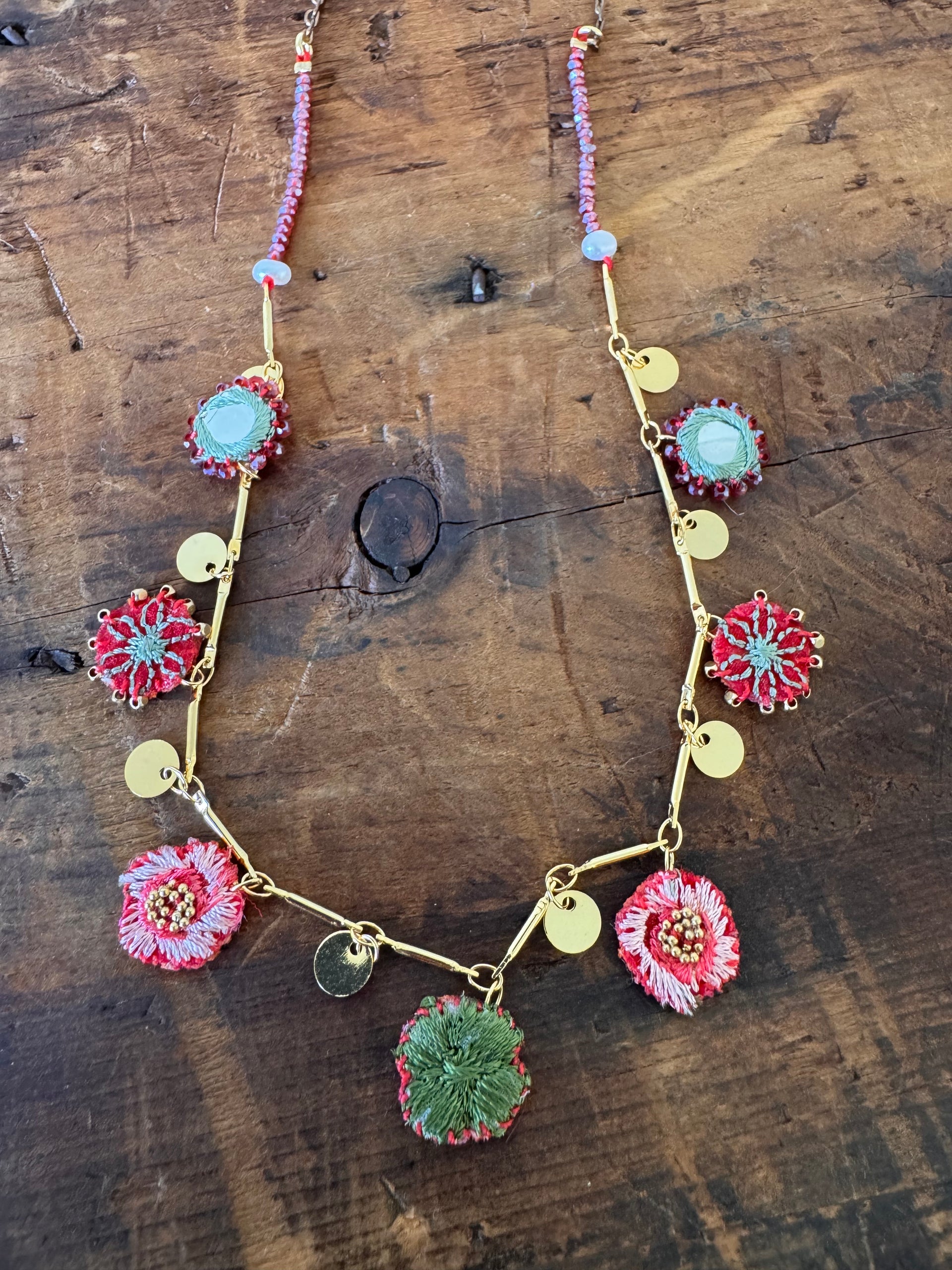 Decorative necklace with floral and round pendants on a wooden surface