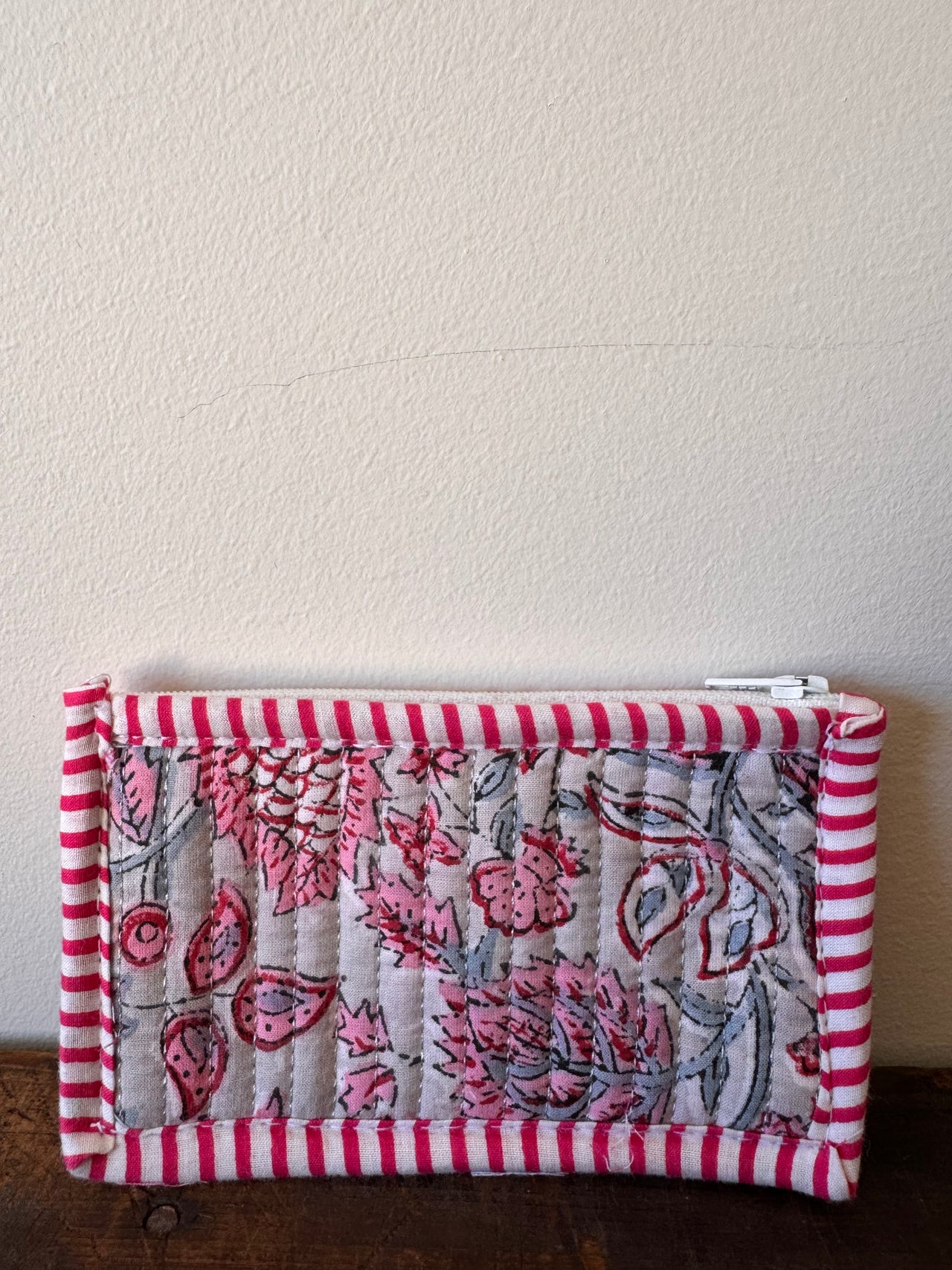 Small pouch with pink floral pattern and red stripes on a textured surface