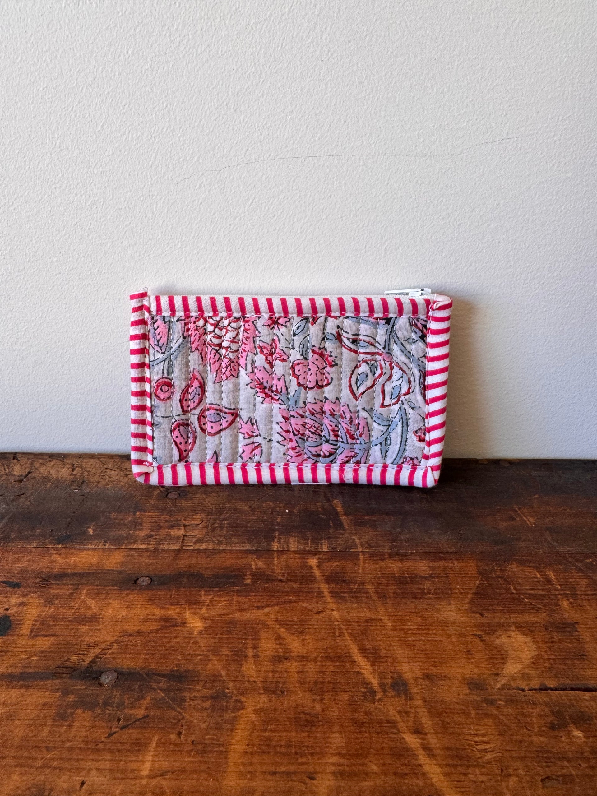 Small quilted fabric square with floral and striped patterns on a wooden surface.