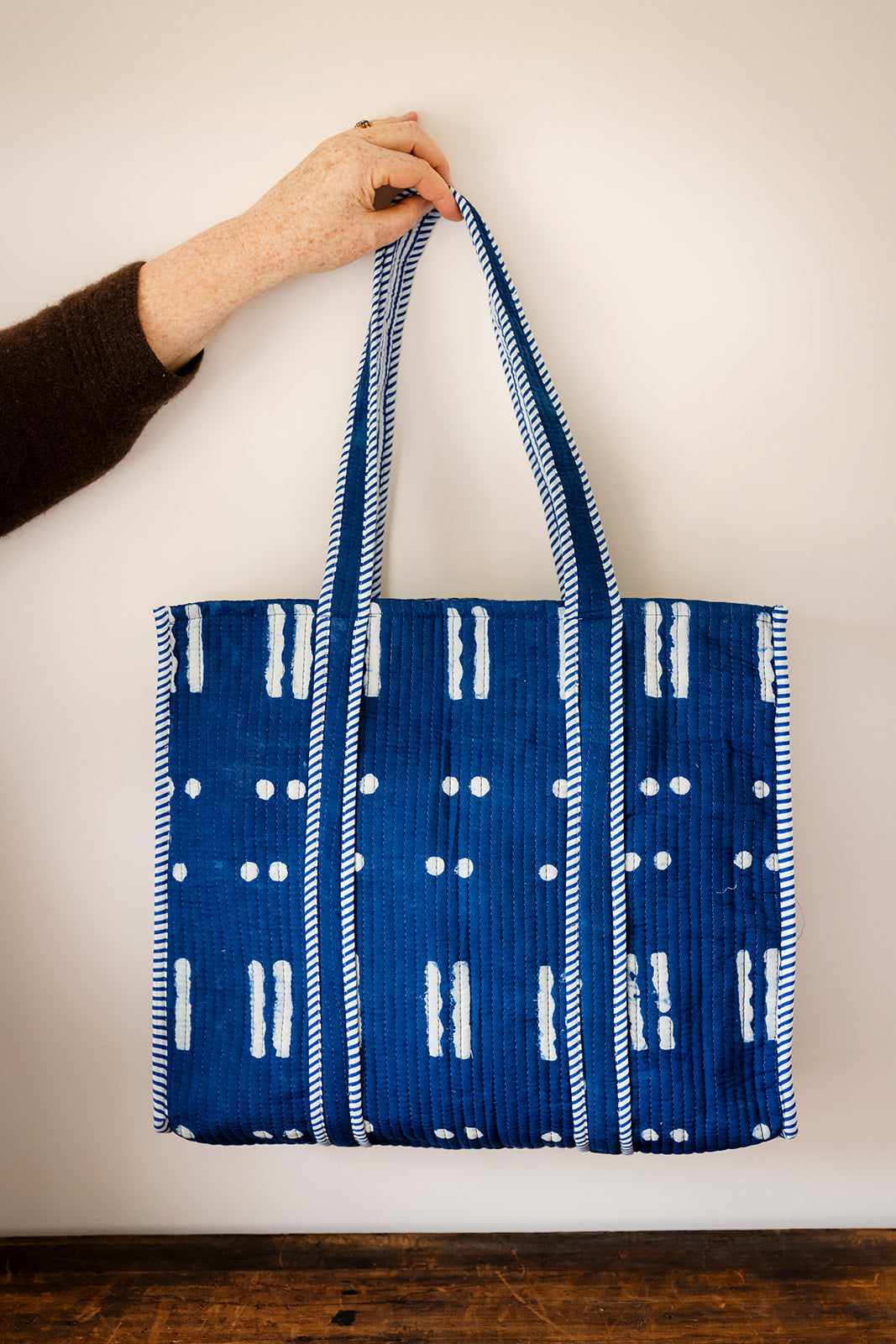 Blue tote bag with white patterns held by a person against a plain background