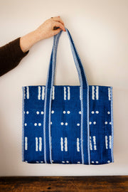 Blue tote bag with white patterns held by a person against a plain background