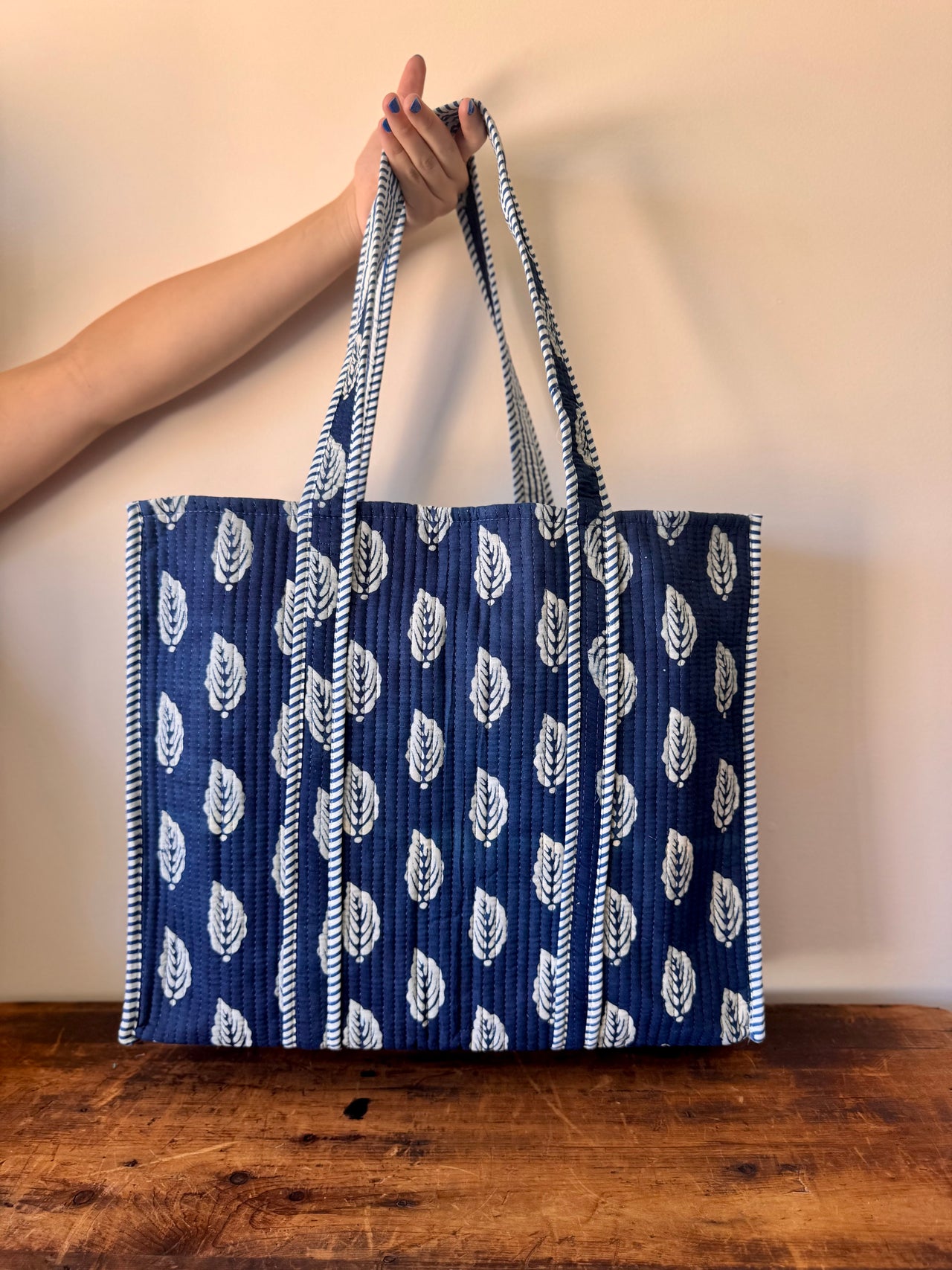 Blue tote bag with white patterns held by a person on a wooden surface.