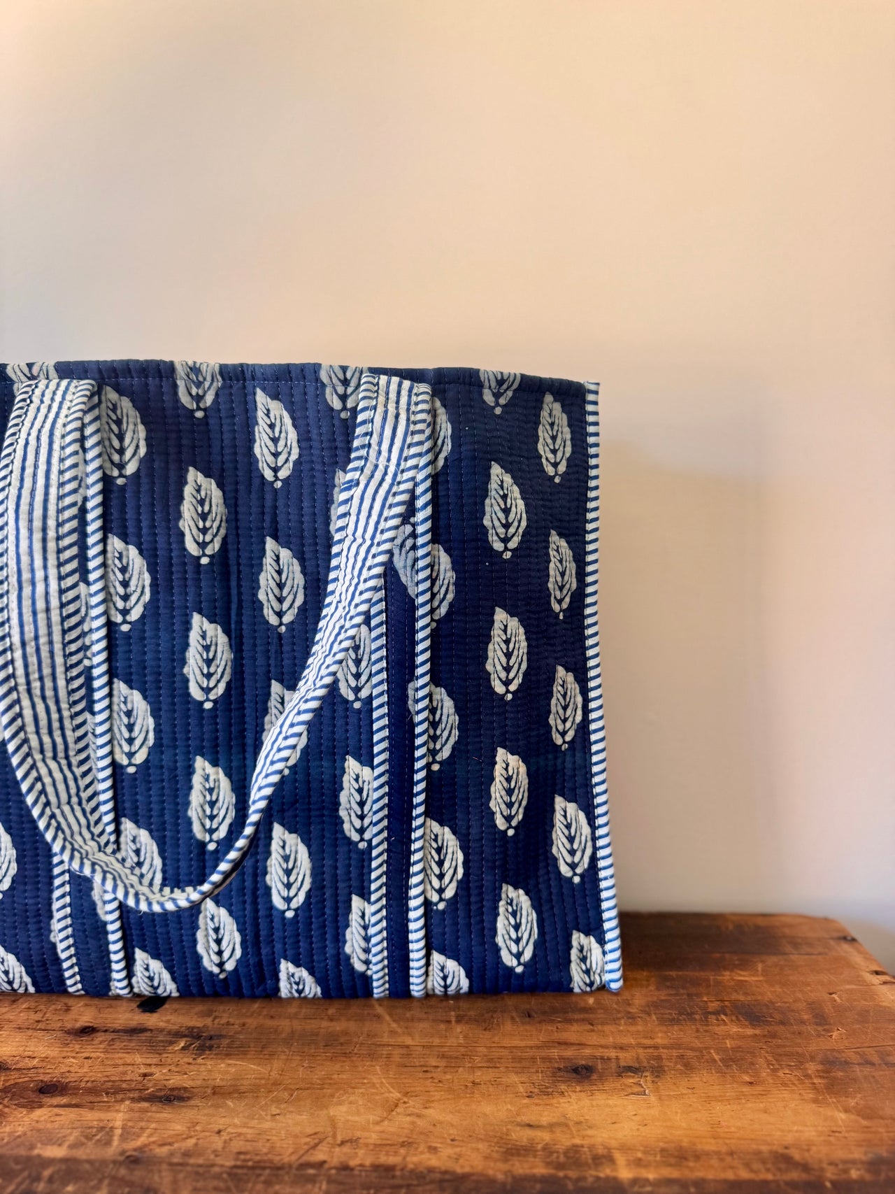 Blue and white patterned bag with a handle on a wooden surface against a beige wall.