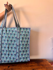 Tote bag with blue floral pattern held by a person against a plain background