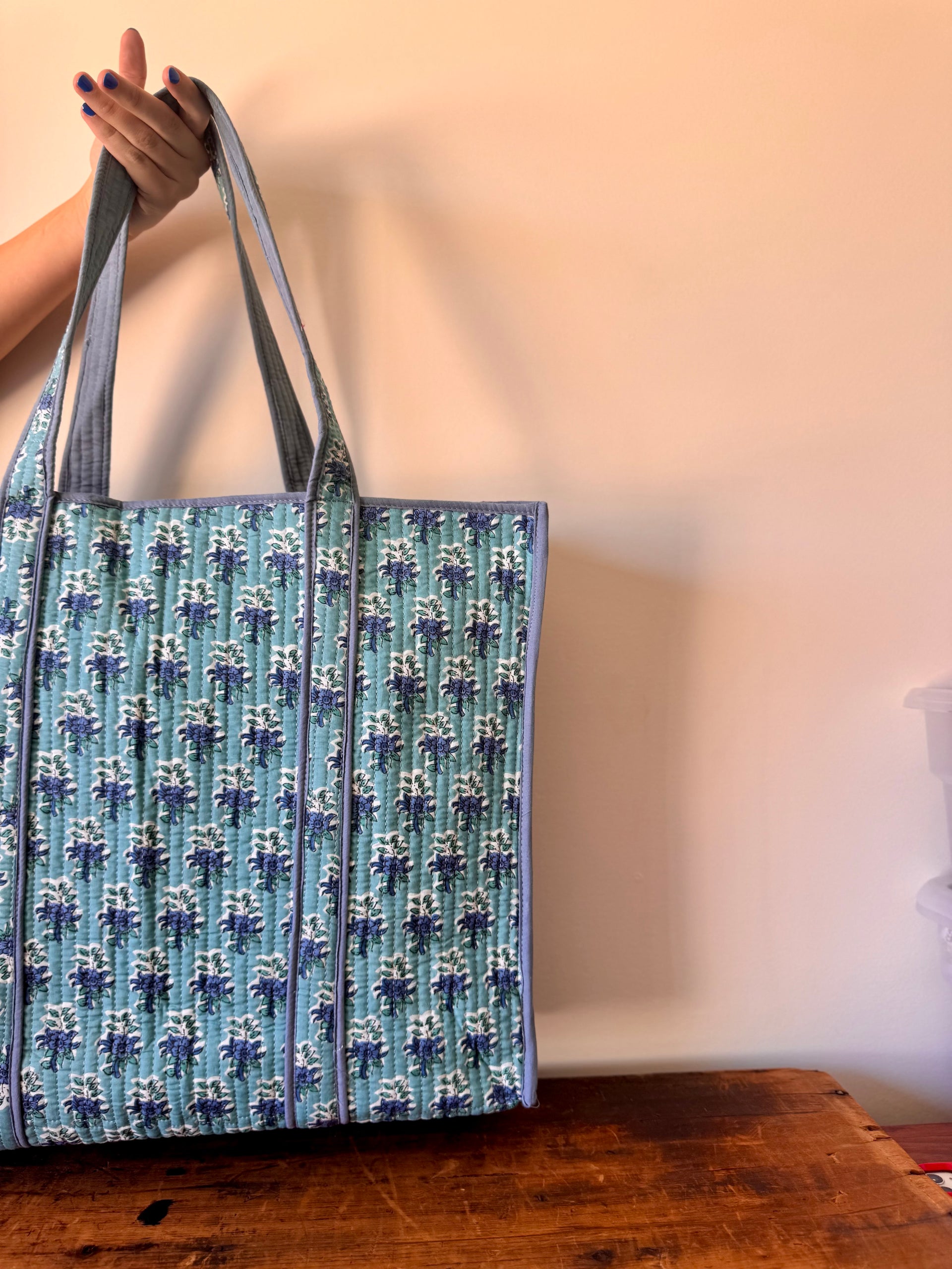Tote bag with blue floral pattern held by a person against a plain background