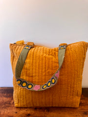 Mustard yellow textured bag with a colorful strap on a wooden surface.
