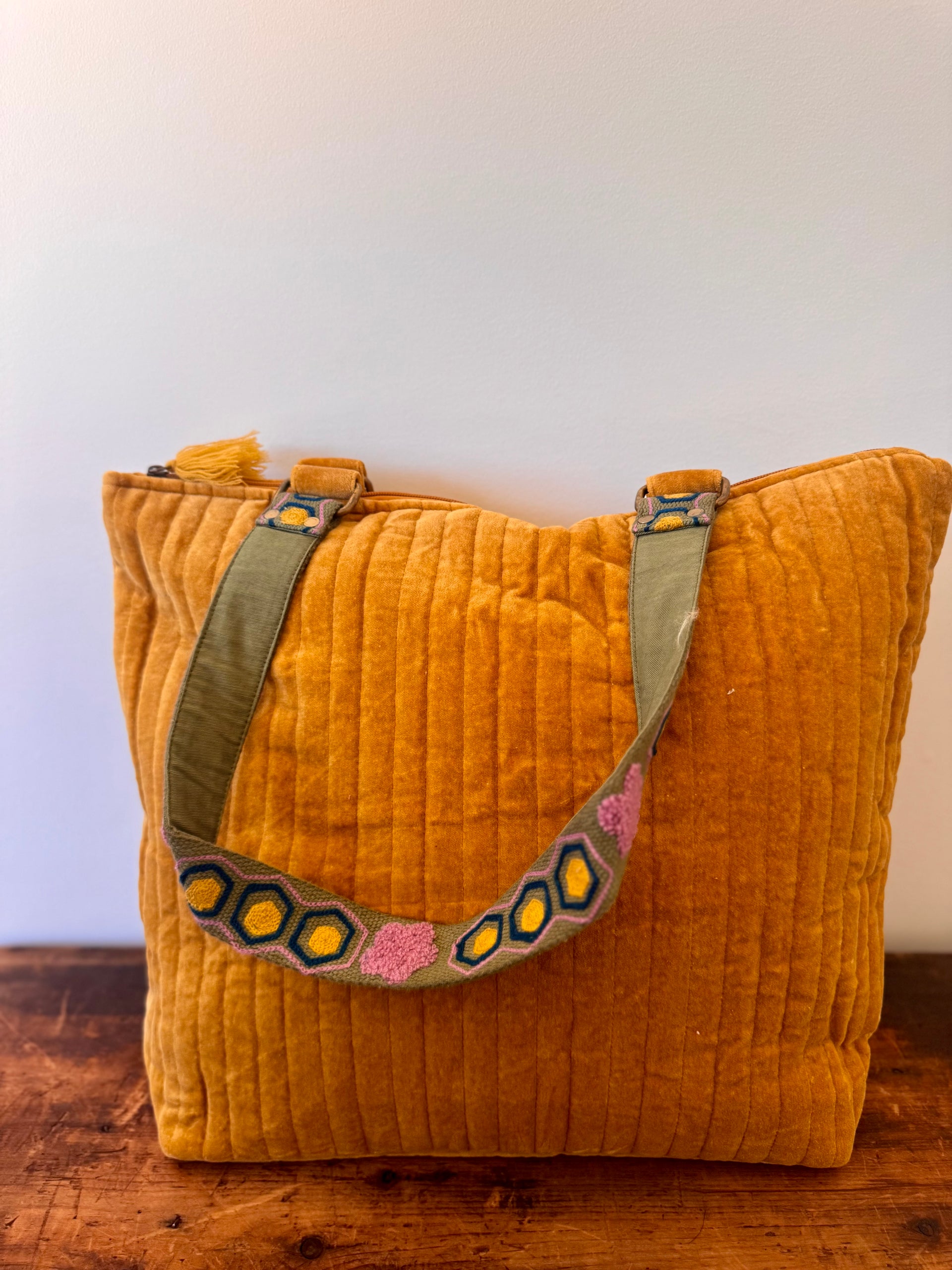 Mustard yellow textured bag with a colorful strap on a wooden surface.