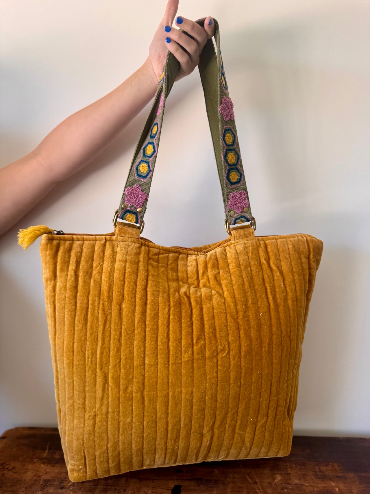 Yellow textured tote bag with a colorful strap held by a person against a plain background