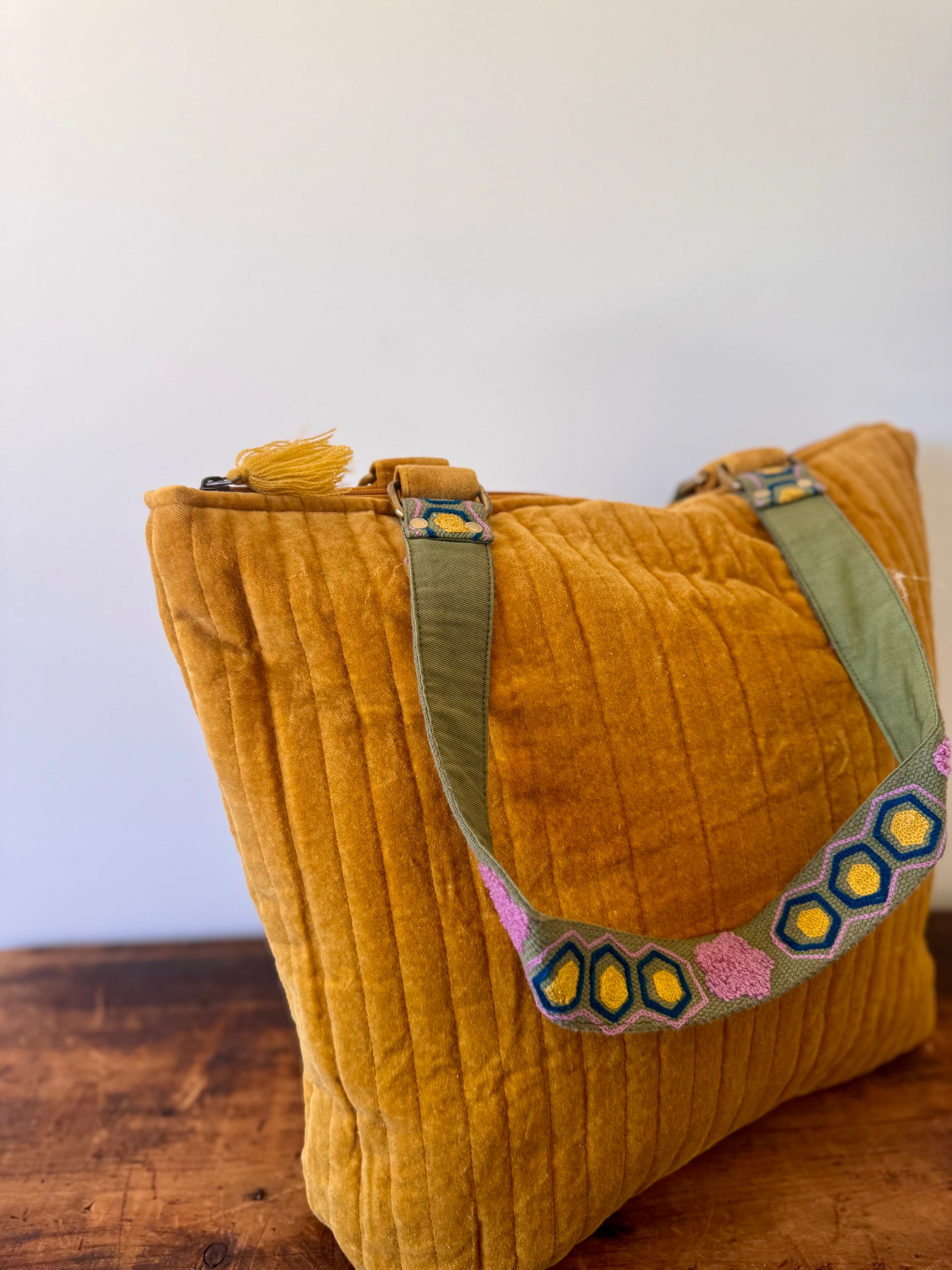 Mustard yellow tote bag with green strap and colorful embellishments on a wooden surface.