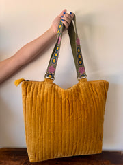 Yellow textured tote bag with a colorful strap held by a person against a plain background