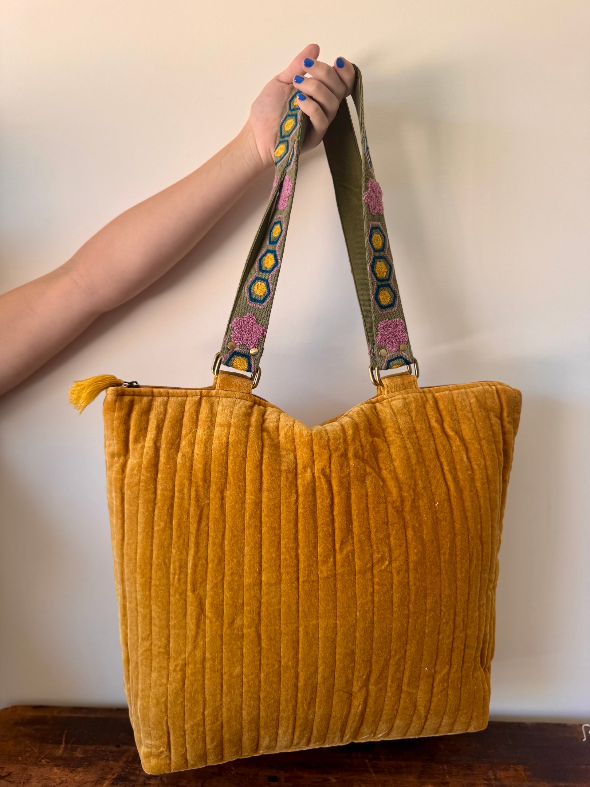 Yellow textured tote bag with a colorful strap held by a person against a plain background