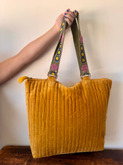 Yellow textured tote bag with a patterned strap held by a person against a plain background