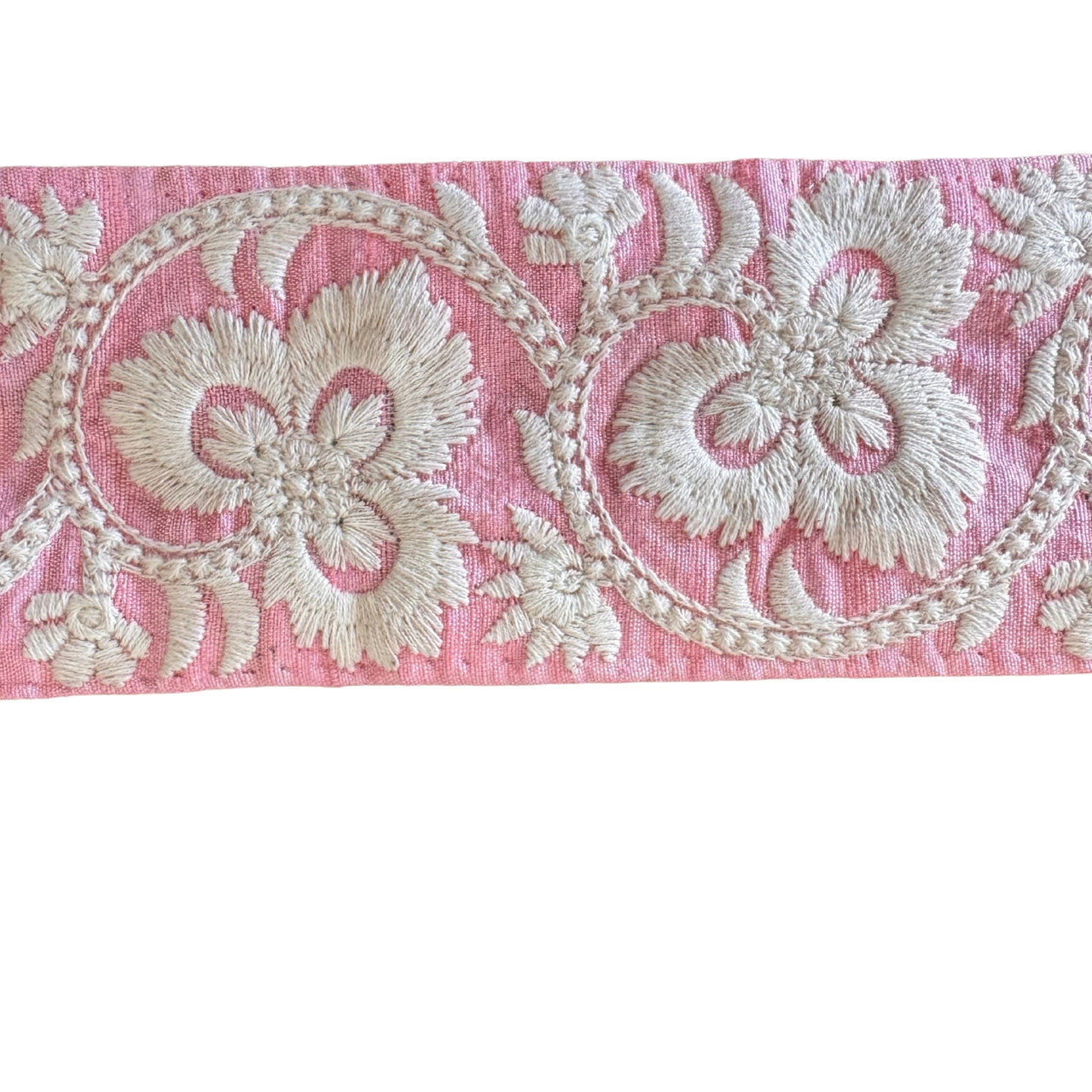 Decorative fabric strip with white floral embroidery on a pink background