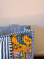 Stack of colorful quilts with floral patterns and blue and white stripes on a neutral background
