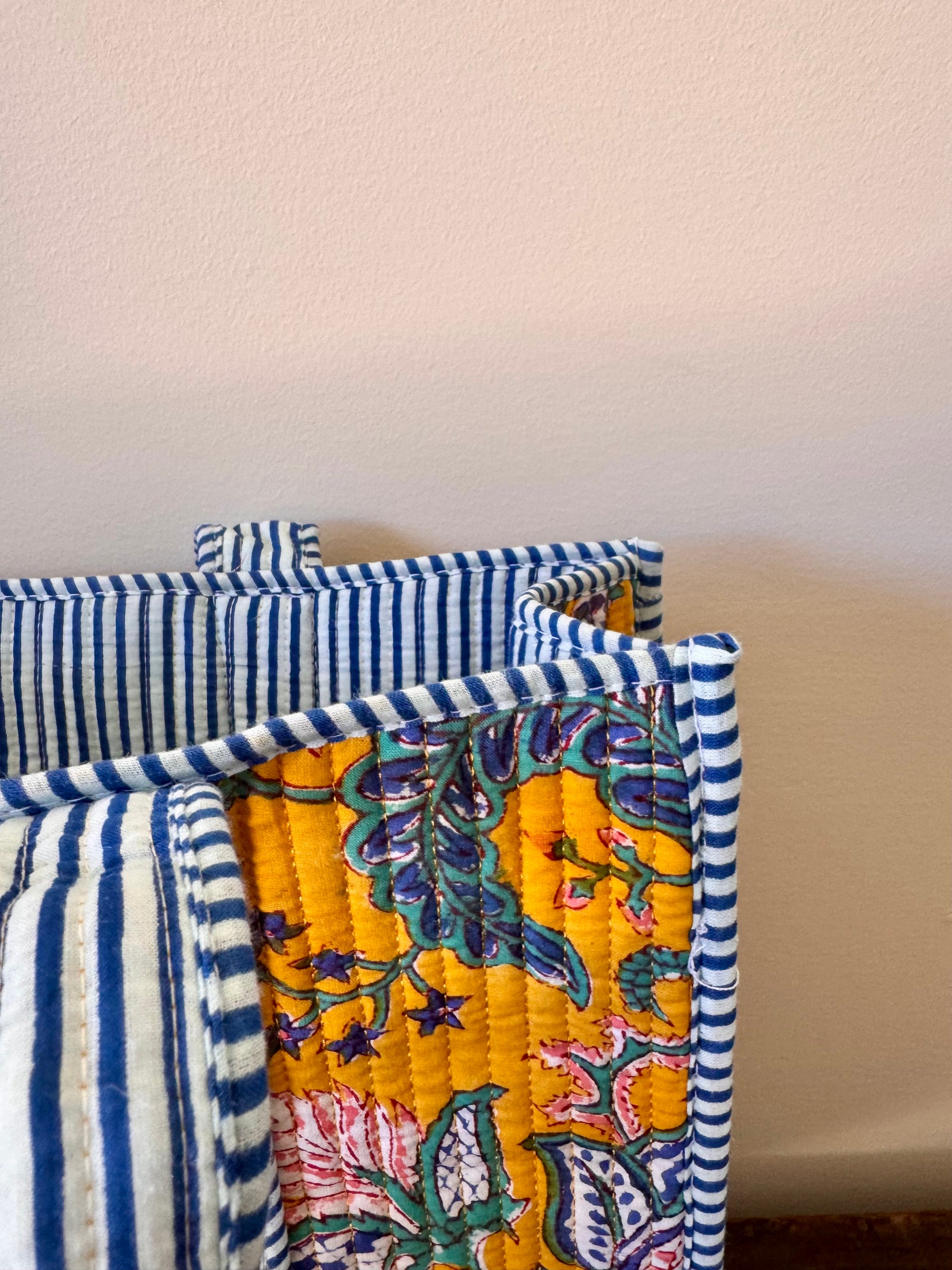 Stack of colorful quilts with floral patterns and blue and white stripes on a neutral background