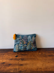 Floral-patterned pouch with a yellow tassel on a wooden surface against a white wall