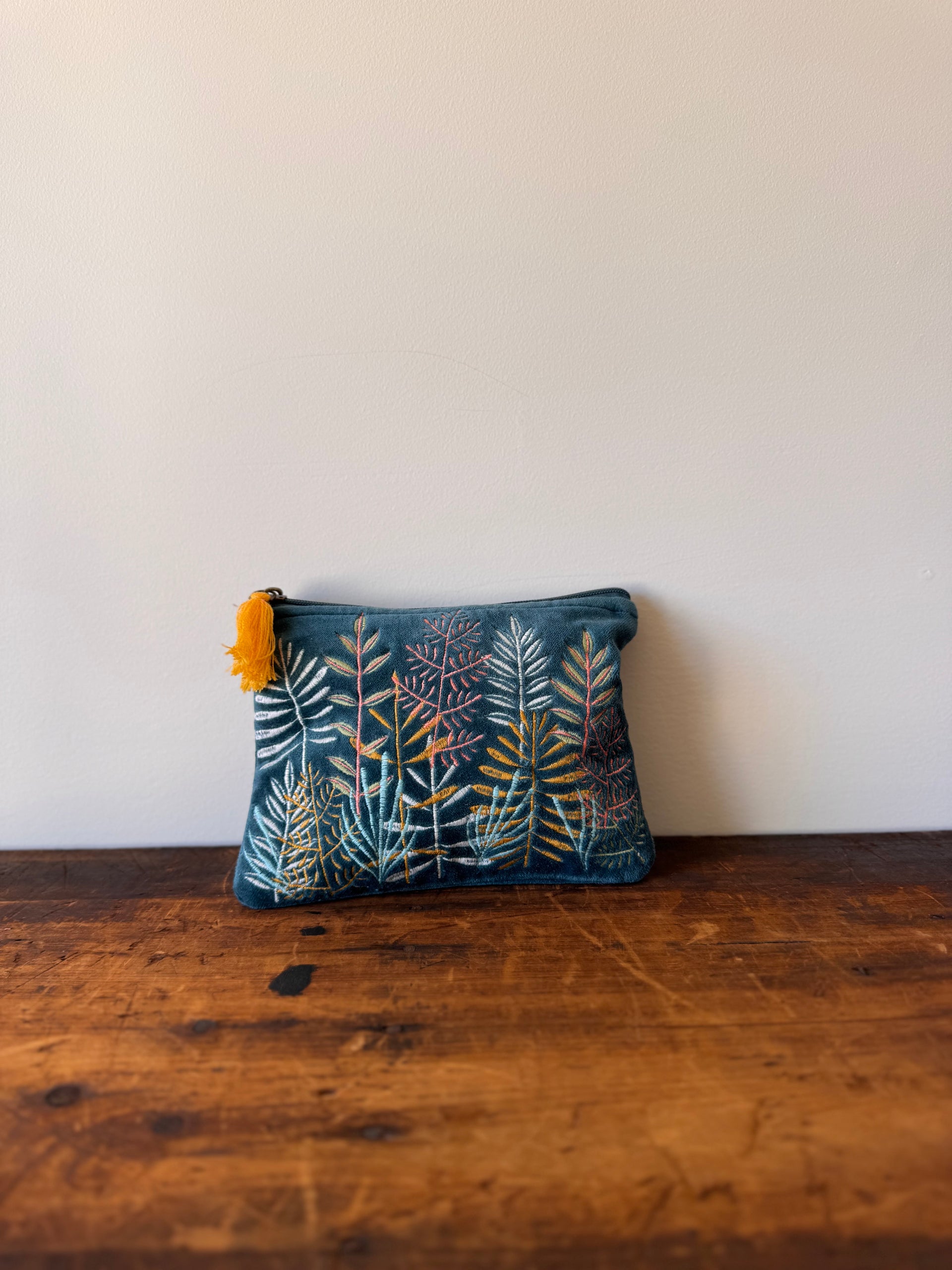 Floral-patterned pouch with a yellow tassel on a wooden surface against a white wall