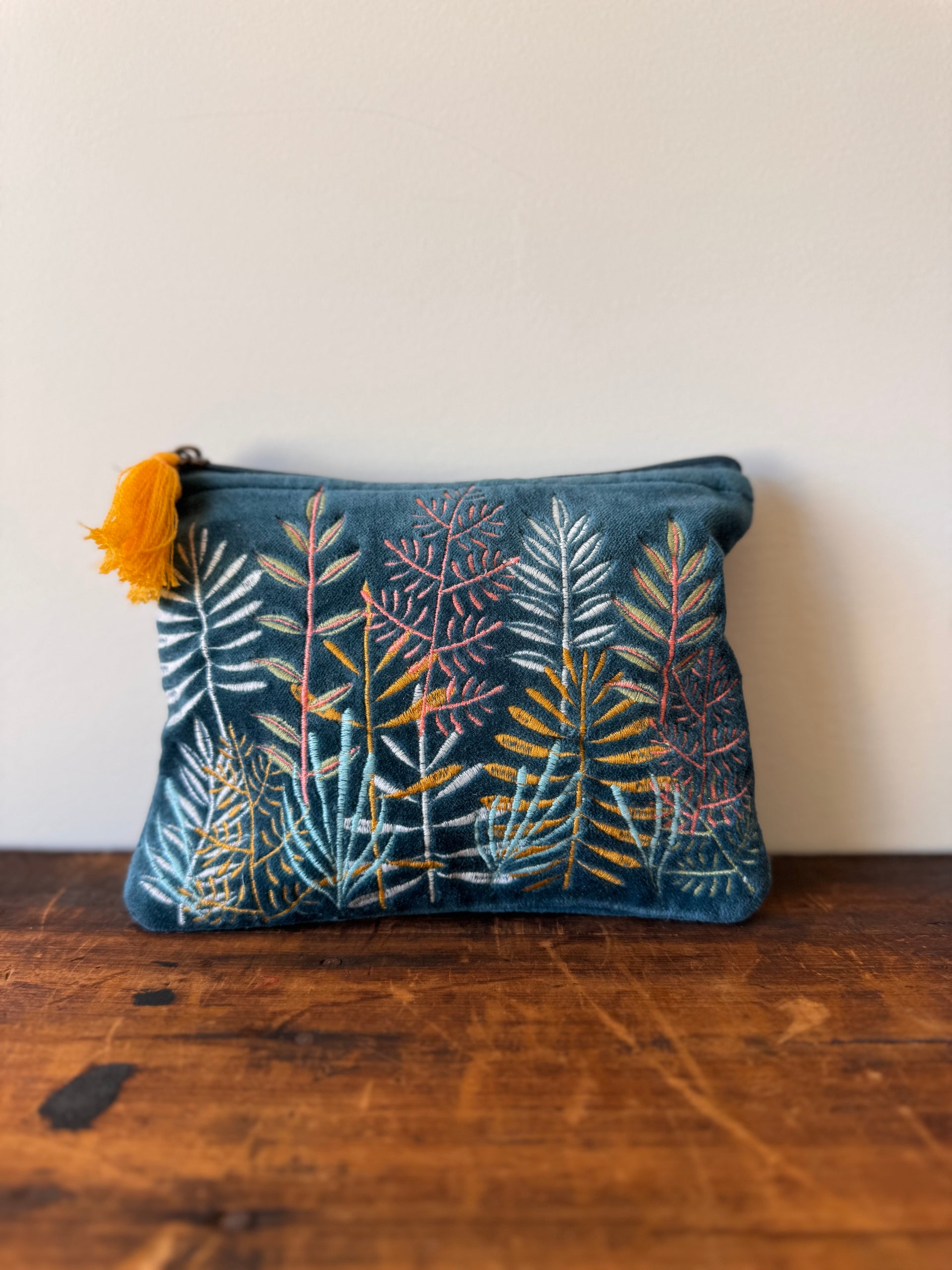 Blue pouch with floral pattern and yellow tassel on a wooden surface