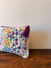 Embroidered pouch with floral pattern and tassel on a wooden surface