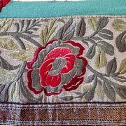 Close-up of embroidered fabric with a red flower and green leaves on a teal background