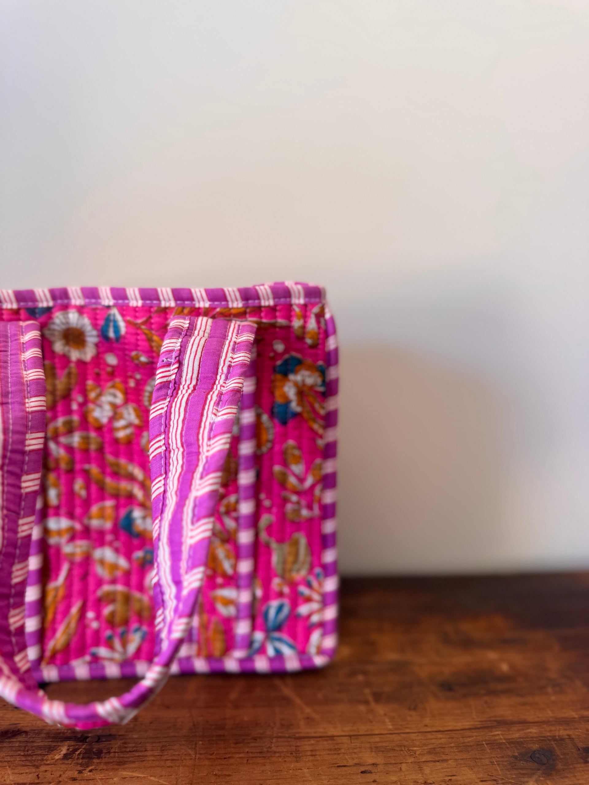 Two pink fabric bags with floral patterns on a wooden surface.