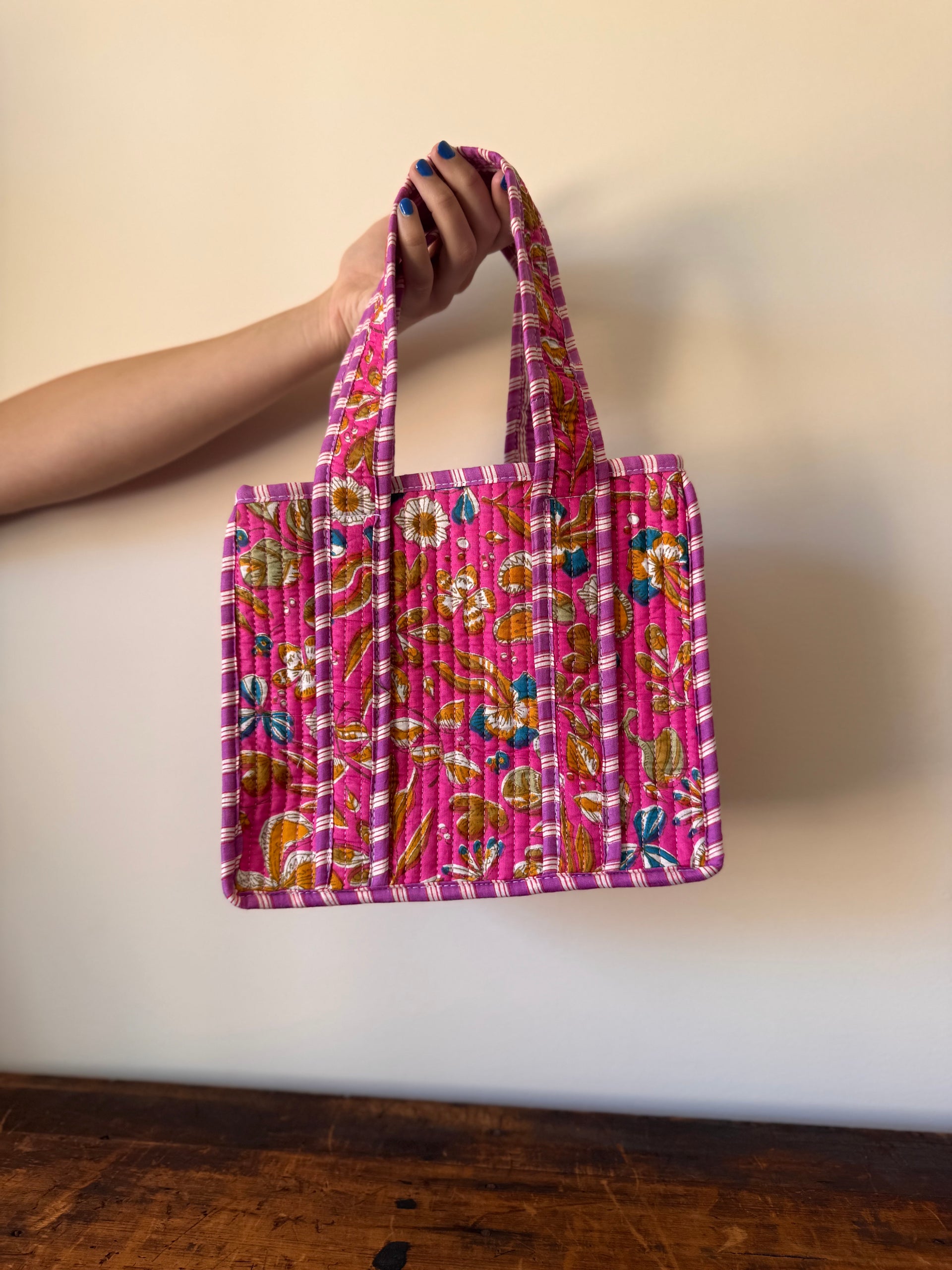 Hand holding a pink patterned bag against a plain background
