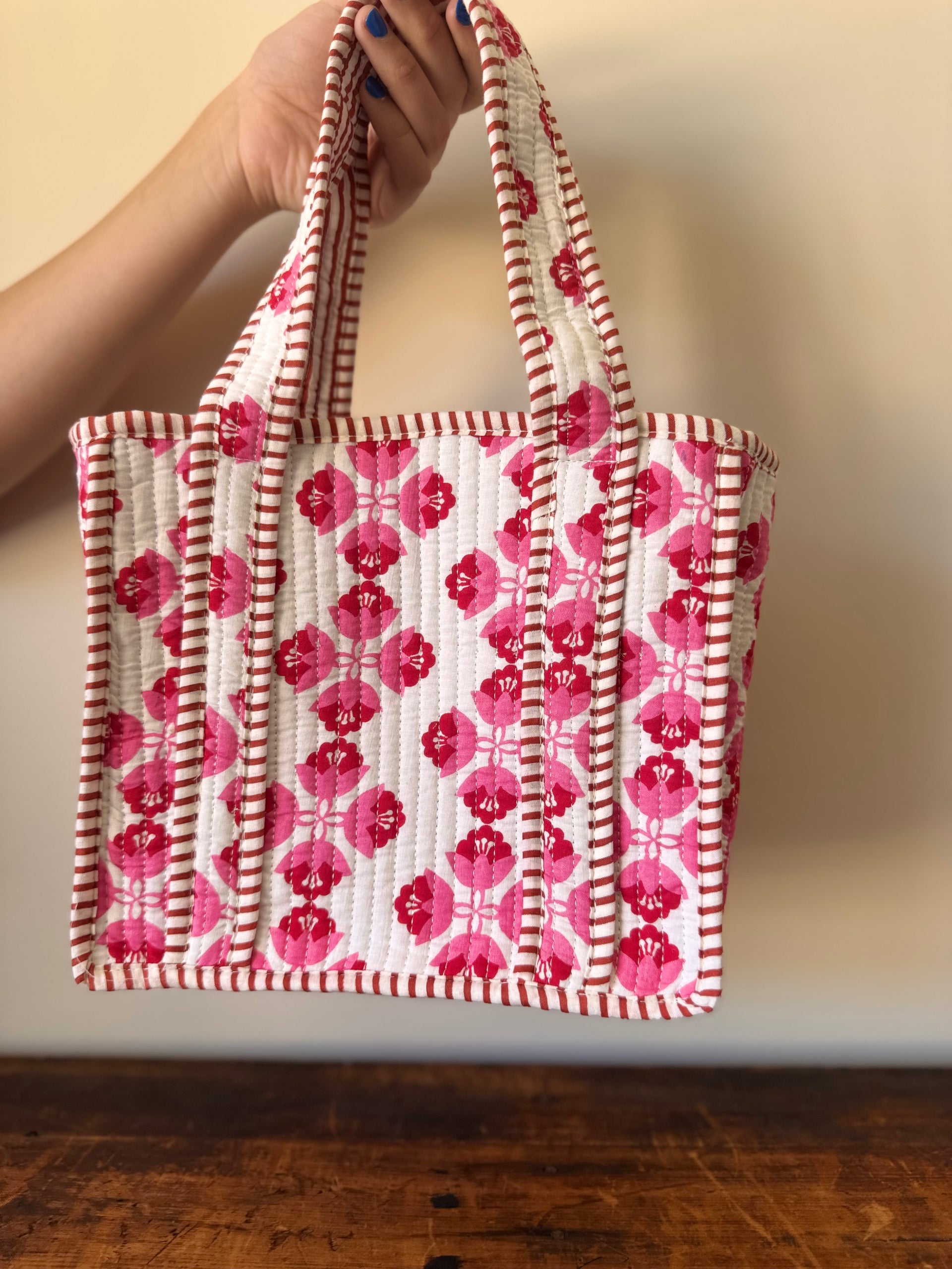 Tote bag with pink floral pattern held by a hand against a neutral background