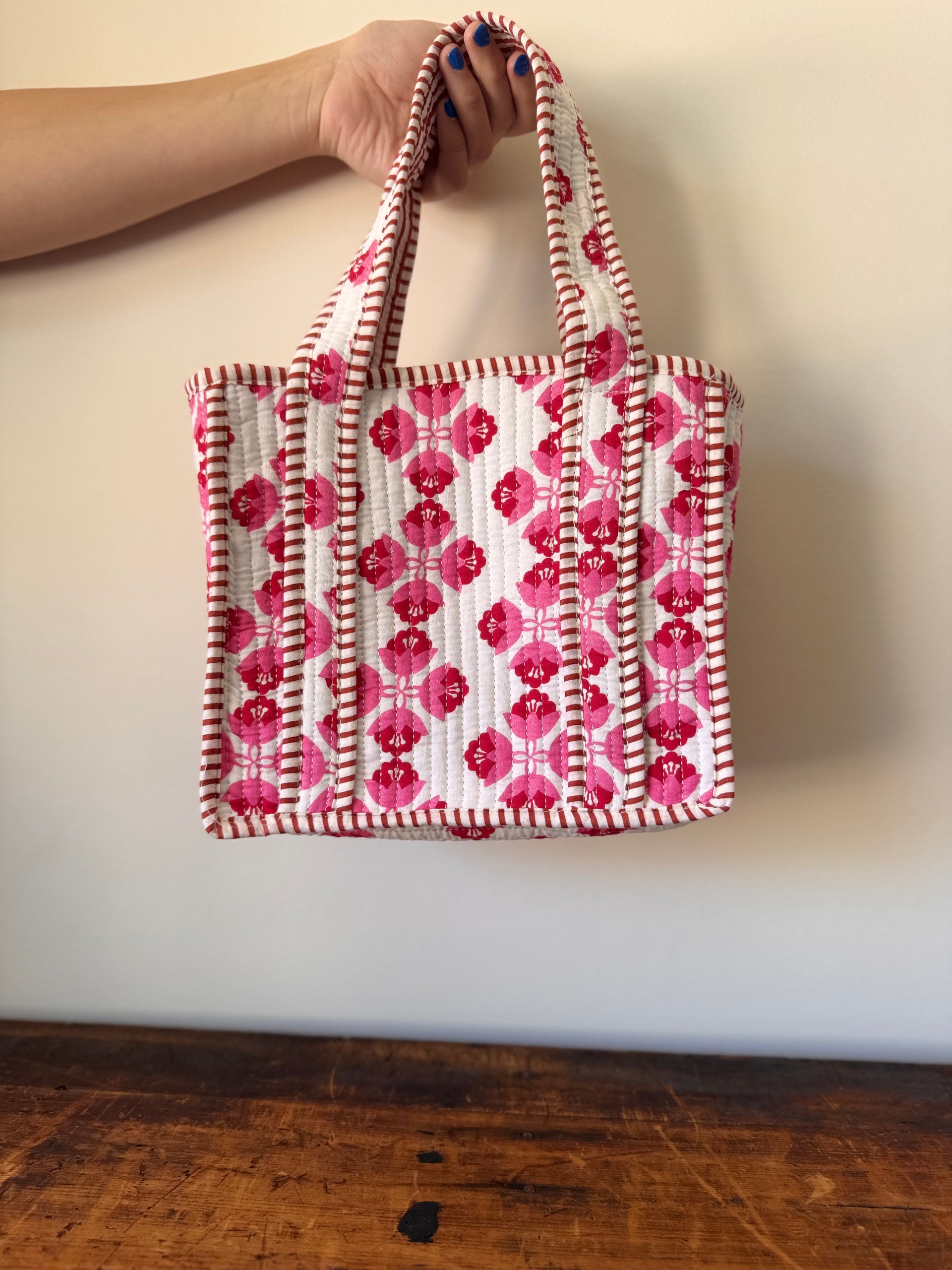 Handbag with pink and white pattern held by a person against a plain background