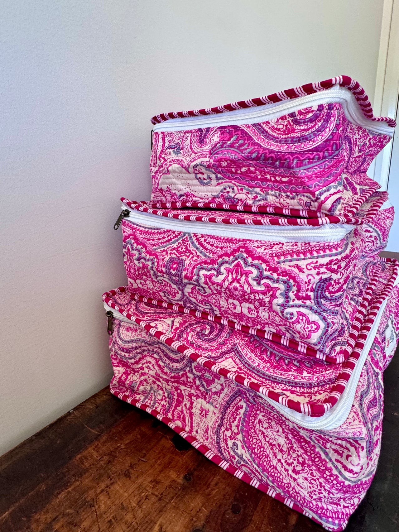 Set of pink and white patterned bags on a wooden floor against a white wall.