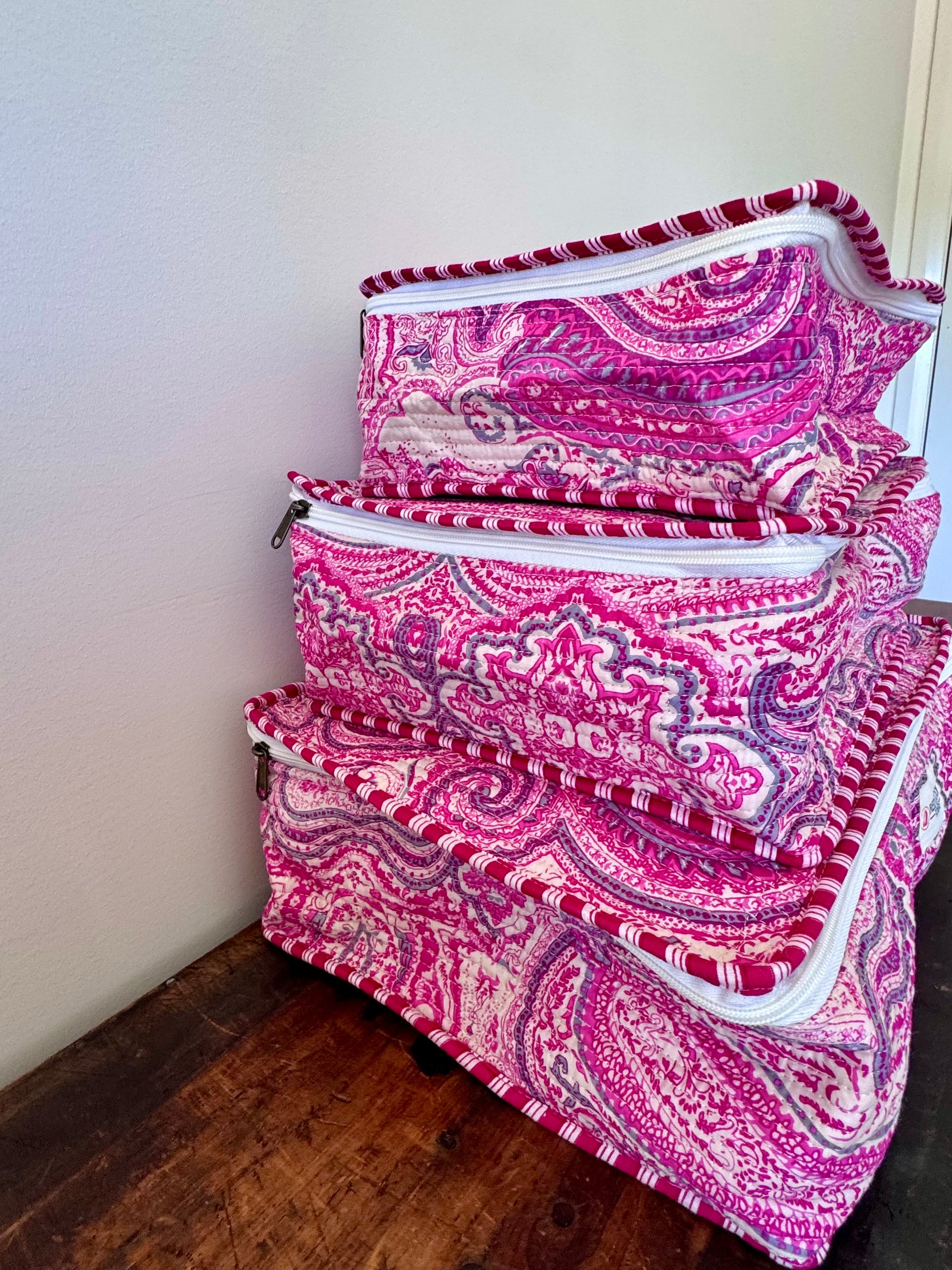Set of pink and white patterned bags on a wooden floor against a white wall.